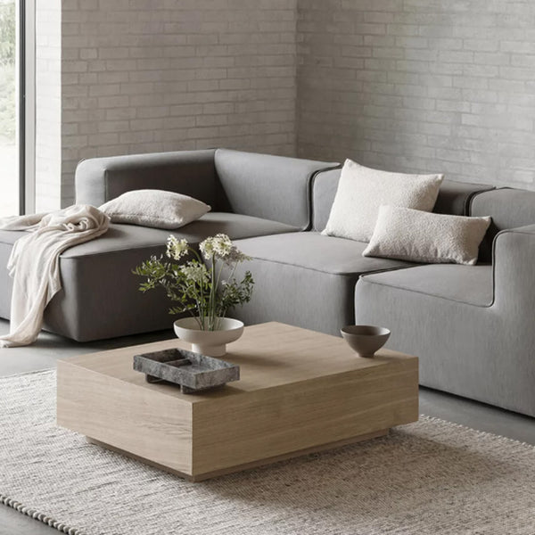  Blomus Wohnzimmer mit grauer Couch, Couchtisch aus Holz und weissen Boucle Kissenhüllen.