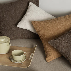 Blomus Boucle Kissenhüllen in braun, creme, und tan auf einer Couch, dekoriert mit einem Holztablett auf dem eine Teekanne und Teetasse im Skandistil stehen.